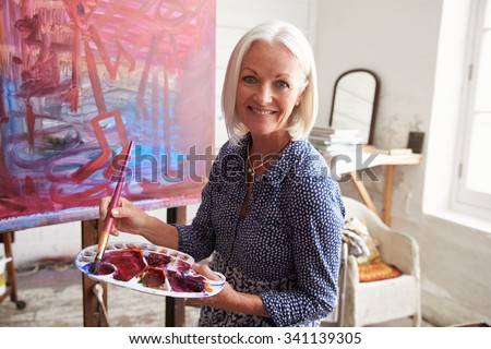 Portrait Of Senior Female Artist Working On Painting In Studio