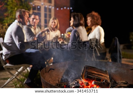 Mature Friends Enjoying Outdoor Evening Meal Around Firepit