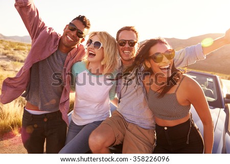 Friends On Road Trip Sitting On Hood Of Convertible Car