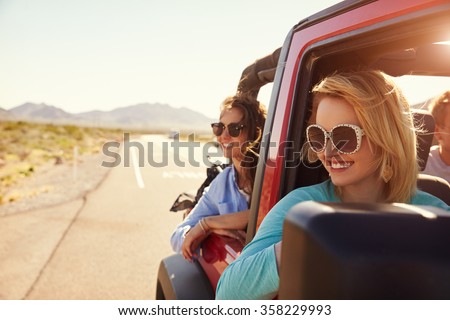 Female Friends On Road Trip In Back Of Convertible Car