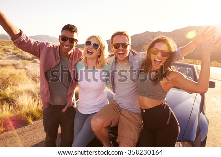 Friends On Road Trip Sitting On Hood Of Convertible Car