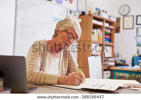 Senior female teacher at her desk marking studentsÃ¢?? work