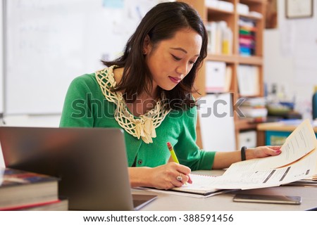 Female Asian teacher at her desk marking studentsÃ¢?? work