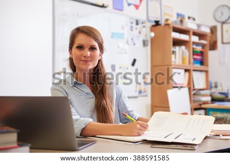 Portrait of young female teacher at desk looking to camera