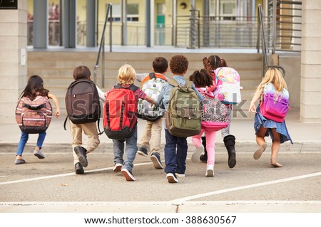 Elementary school kids running into school, back view
