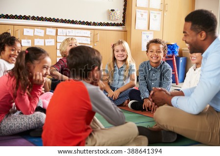 Elementary school kids and teacher sit cross legged on floor