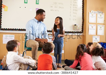 Schoolgirl at front of elementary class talking with teacher