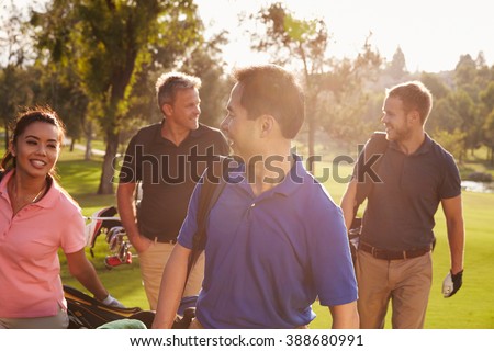 Group Of Golfers Walking Along Fairway Carrying Golf Bags