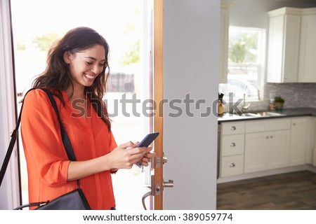 Woman Checking Mobile Phone As She Opens Door Of Apartment