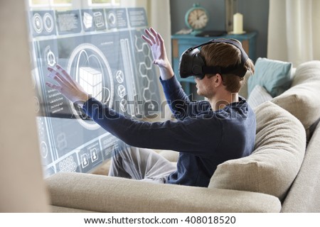 Man Sitting On Sofa At Home Wearing Virtual Reality Headset