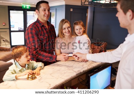 Family Checking In At Hotel Reception Desk