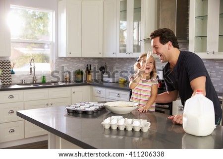 Dad laughs as girl puts cake mix on his nose in the kitchen