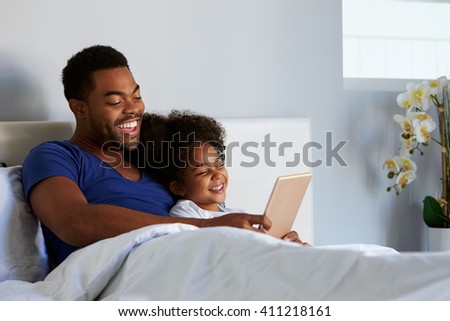 Black father and daughter relax in bed with tablet computer