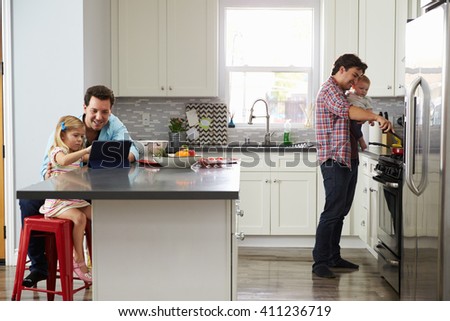 Girl uses tablet in kitchen with dad, while other dad cooks