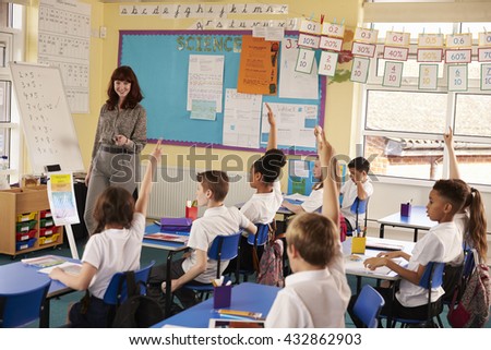 Primary school kids raising hands in class to answer teacher
