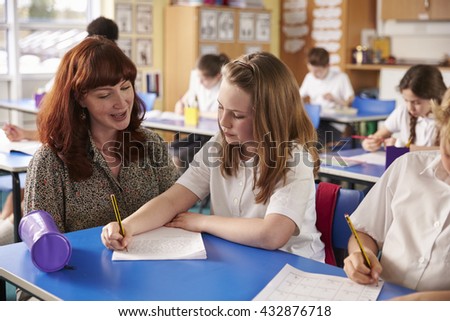 Primary school teacher helping a girl writing at her desk