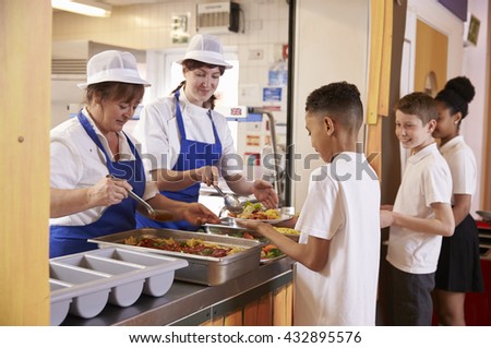 Two women serving food to a boy in a school cafeteria queue