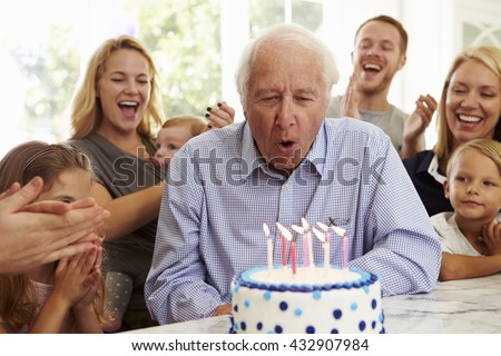 Grandfather Blows Out Birthday Cake Candles At Family Party