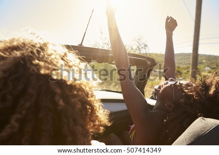 Young couple in an open top car, woman with arms raised