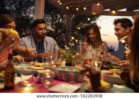 Friends eat and talk at a dinner party on a patio, close up