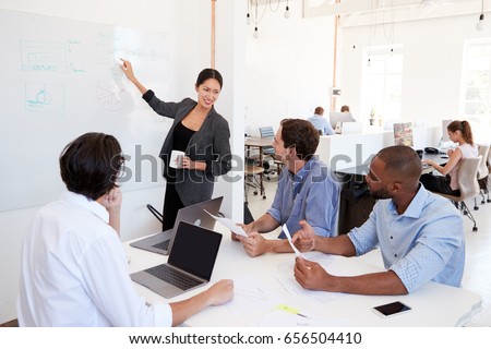 Woman pointing at whiteboard at a meeting in a busy office
