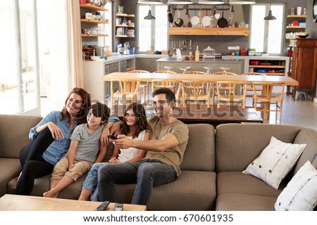 Family Sitting On Sofa In Open Plan Lounge Watching Television