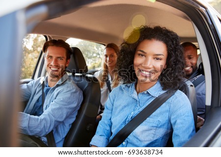 Four adult friends in a car on a road trip smiling to camera