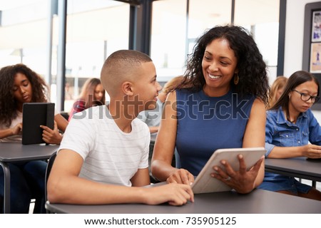 Teacher helping teenage schoolboy with tablet computer