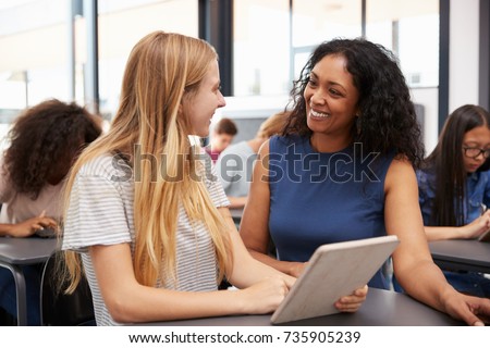 Teacher helps blonde teenage schoolgirl with tablet computer