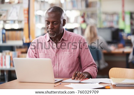 Mature Male Student Working On Laptop In College Library