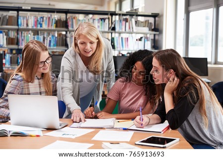 Woman Teacher Working With Female College Students In Library