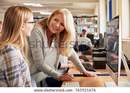 Teacher With Female Student Working On Computer In College Library