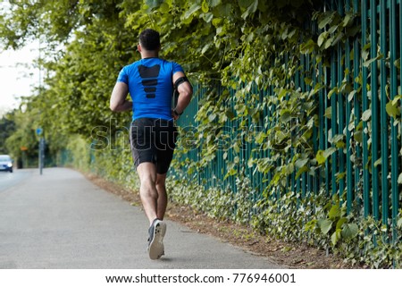 Back view of young male athlete running in the street