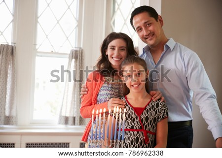 Jewish parents and daughter smiling, lit candles on menorah