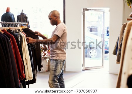 Young black man browsing through clothes on a rail in a shop