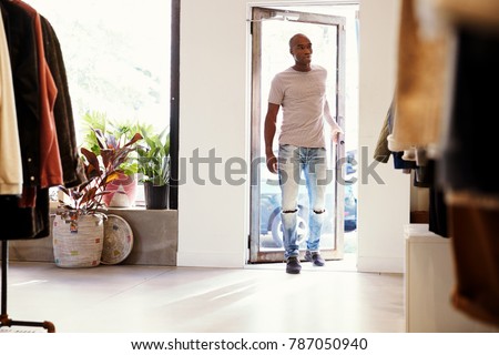 Young black man walking into a clothes shop and closing door
