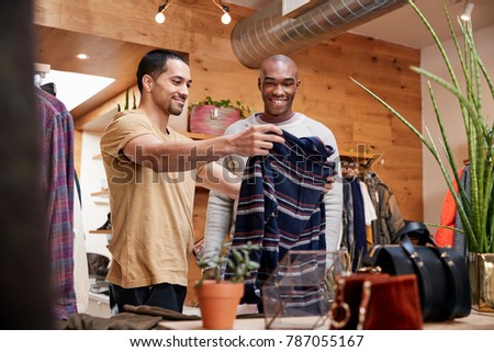 Two young men holding up clothes to look at in clothes shop