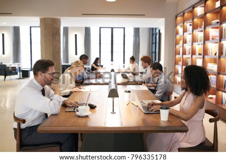 Colleagues at desks in a busy open plan office, close up