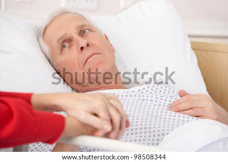 Senior man in hospital bed holding wife\'s hand