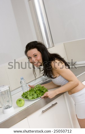 young caucasian brunette in gym wear,showing a salad dish smiling in her kitchen.Concept of healthy lifestyle with a correct diet.