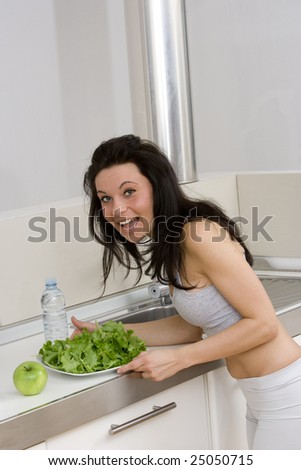 young caucasian brunette in gym wear,showing a salad dish smiling in her kitchen.Concept of healthy lifestyle with a correct diet.