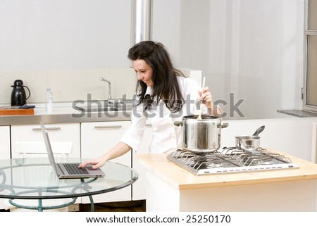 young caucasian brunette working with laptop while cooking in her kitchen.Concept of on line receipt,hard working.