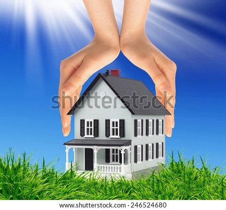 house between  hands representing home ownership and the real estate business against blue sky