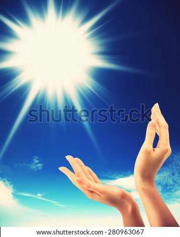 Bright sun between two hands over blue sky showing freedom or solar power concept