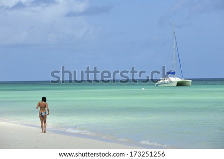 A woman walking along tropical beach with white sand and turquoise water, Caribbean Sea