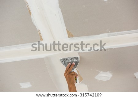 man hand with trowel plastering a ceiling, skim coating plaster walls