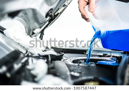 Pouring antifreeze liquid for washing car screen.