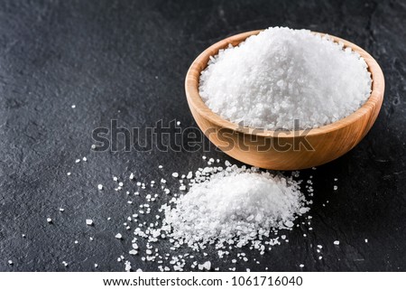 Salt in wooden olive bowl on stone table. Salt top view. Sea salt on black background.