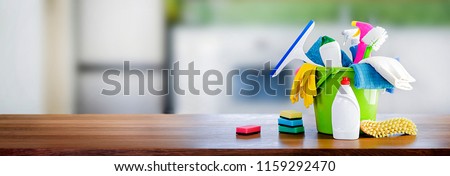 Bucket with cleaning items on wooden table and blurry modern kitchen background. Washing set colorful with copy space banner.