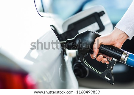Woman pumping petrol at gas station into vehicle. Hand holding a pistol or nozzle pump prepare to refuel car with gasoline.